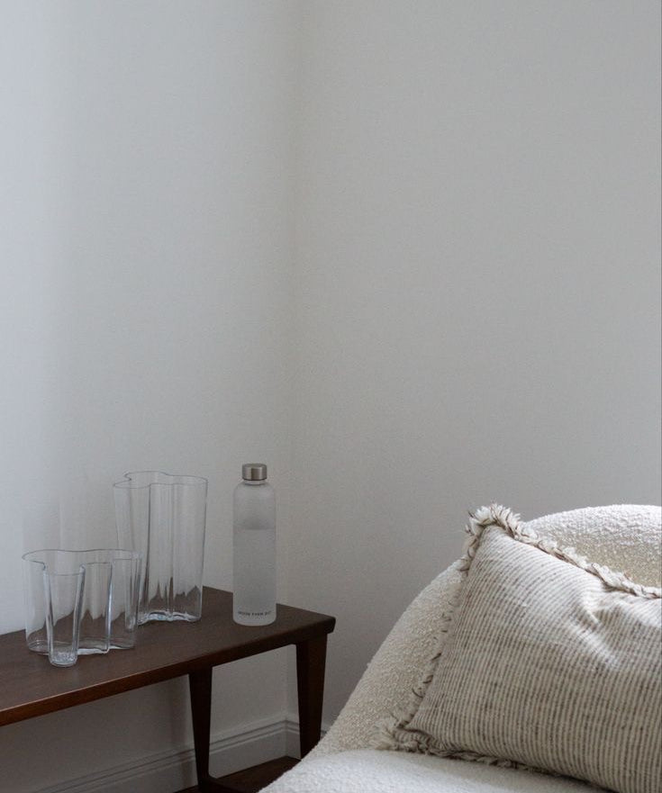 The Water-Tracking Bottle sits on a wooden desk beside a cream chair