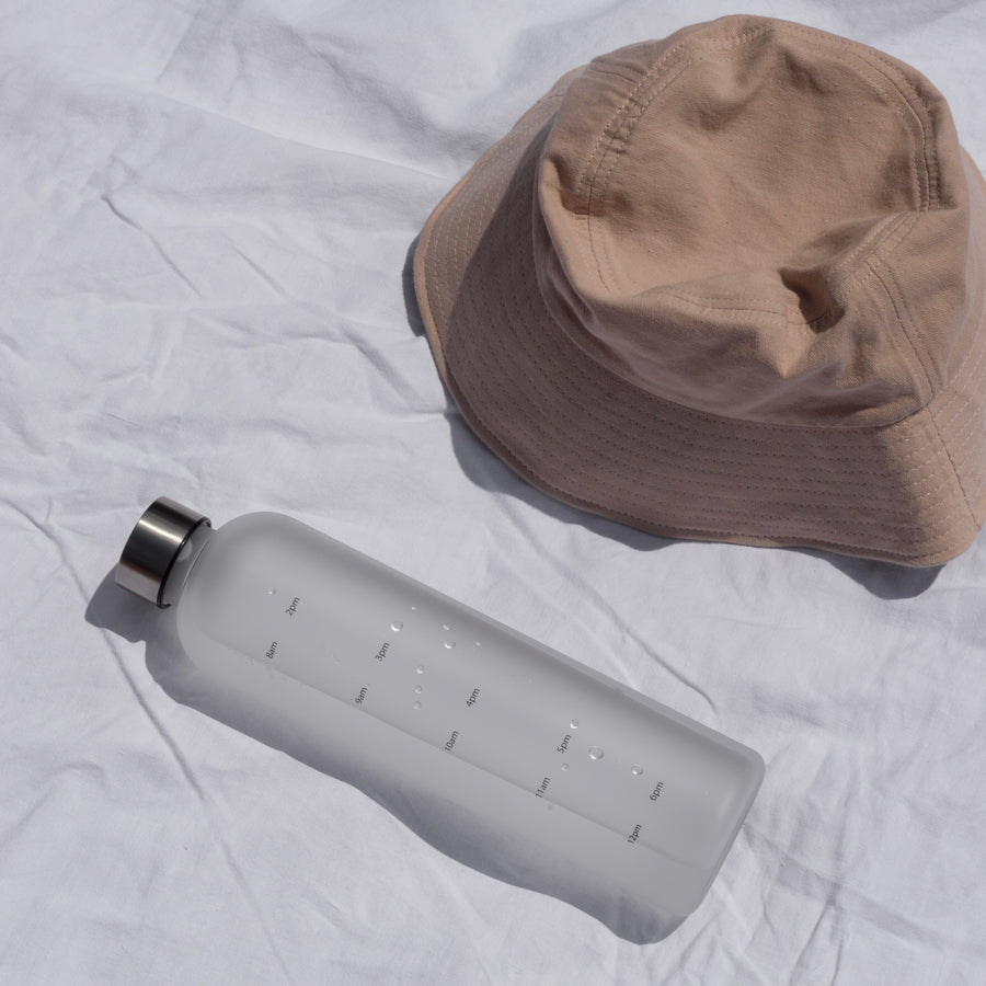 Water tracking bottle on white sheet next to brown hat